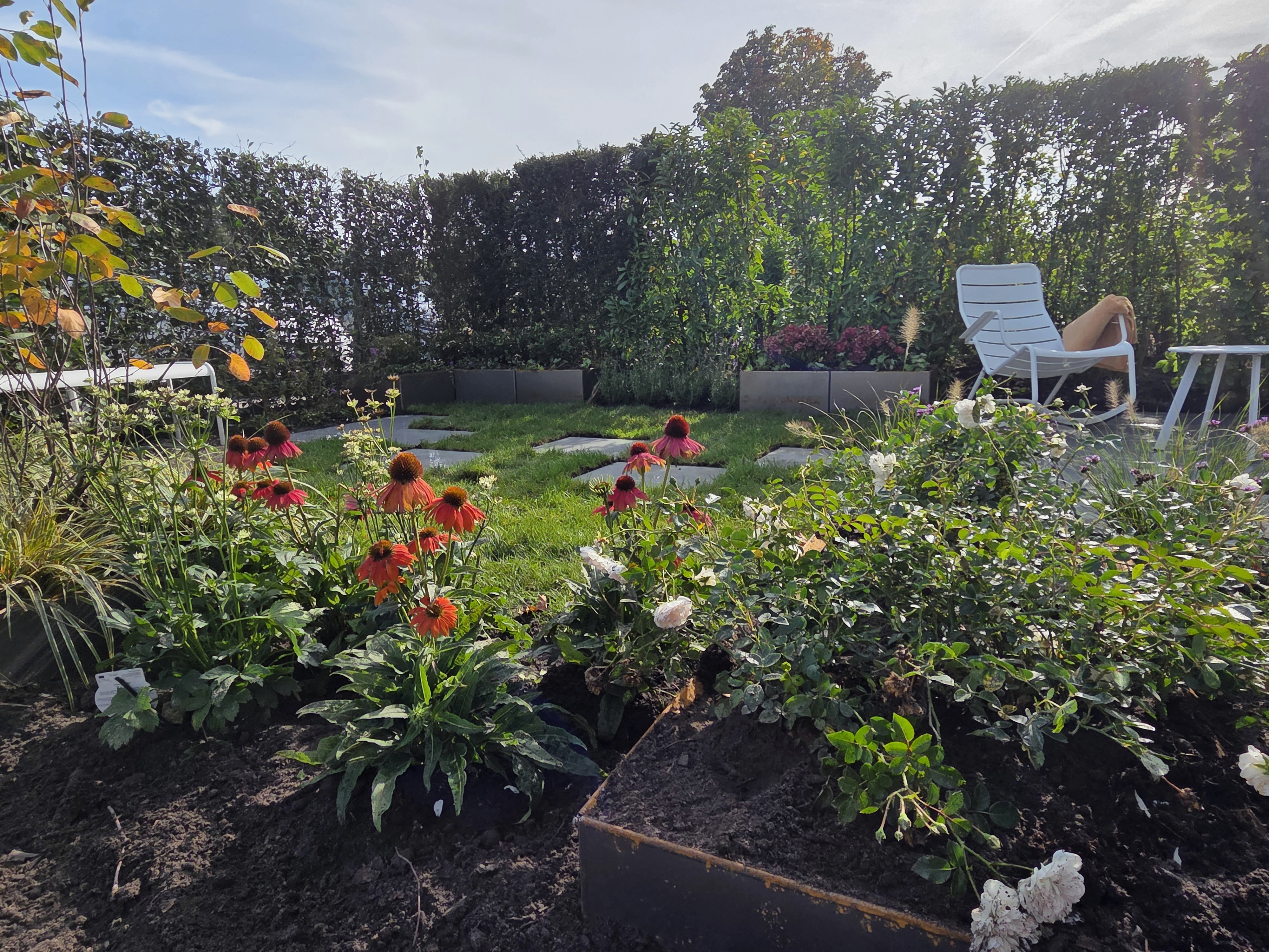 Tuin met kleurrijke beplanting, gras, staptegels en een zithoek als toepassing van het Preverde systeem